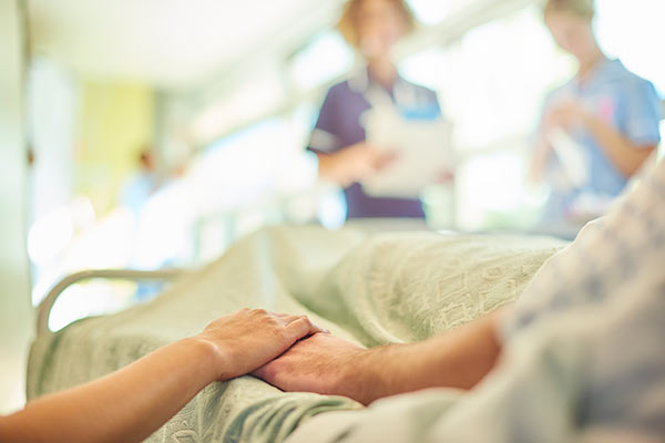 daughter holding mothers hand in hospital bed